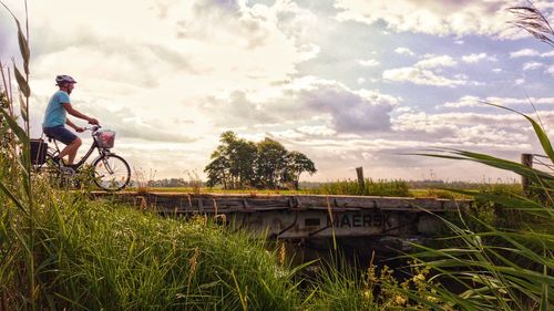 Man riding bicycle on field against sky