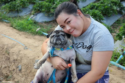 High angle portrait of smiling woman with pug sitting on field