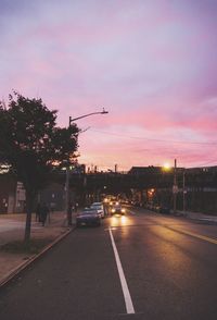 Cars on street against sky at sunset