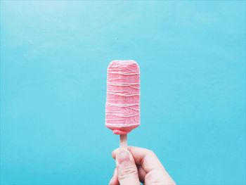 Close-up of cropped hand holding pink popsicle against blue sky