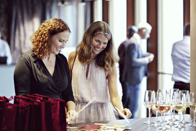 Smiling businesswomen looking at props by wineglasses on table in office party