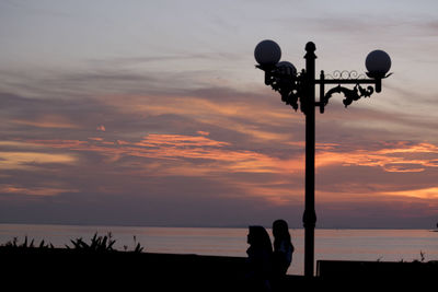 Silhouette people walking by beach against sky during sunset