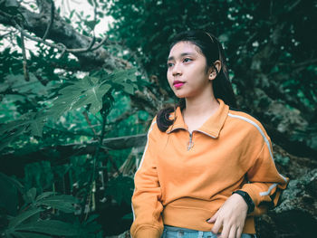 Young woman looking away while standing against trees