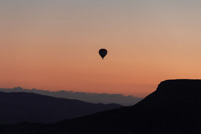 Silhouette hot air balloon flying over mountains against clear sky during sunset