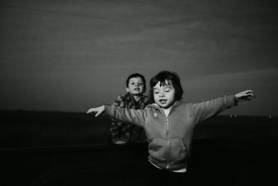 Siblings playing on field against sky at dusk