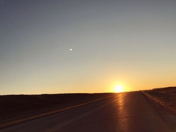 Road amidst field against sky during sunset