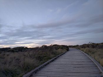 Boardwalk on field against sky