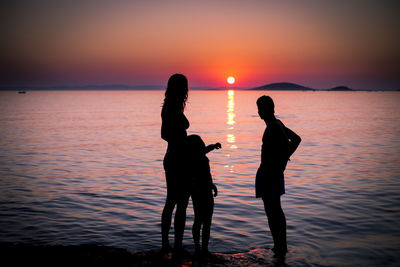 Silhouette of people standing at beach during sunset