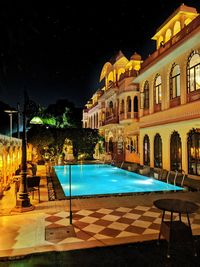 View of swimming pool by building at night