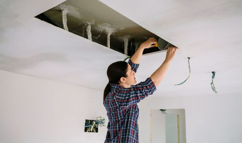 Low angle view of woman repairing ceiling at home