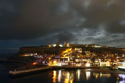 Illuminated cityscape by sea against sky at night