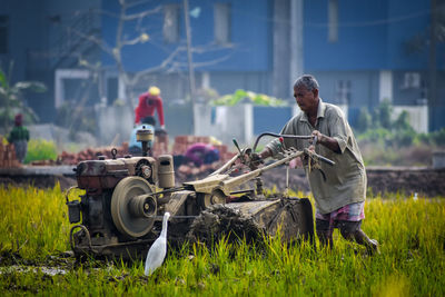 An old farmer is digging soil with tractor in field 