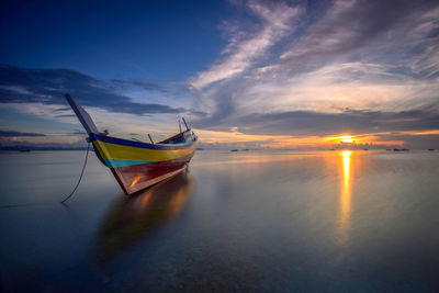 Boat moored in sea against sky during sunset