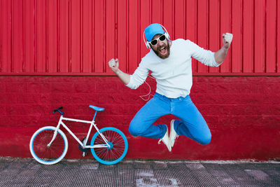 Full length of young man with bicycle on red wall