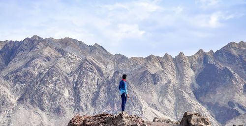 Boy standing on rock against mountains and sky