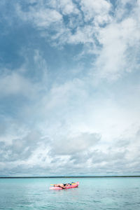 Woman relaxing on canoe in scenic sea against sky