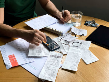 Man is making audit of household expenses using calculator and notebook. lots of receipts and bills