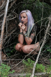 Thoughtful woman crouching on field at forest