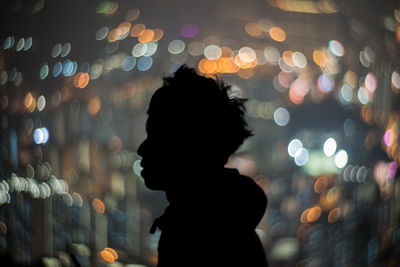 Side view of man standing against defocused lights