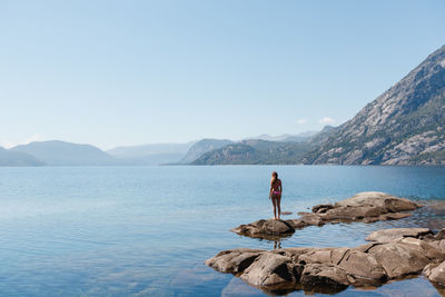 Rear view of man standing by lake against clear sky