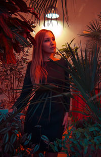 Young woman looking away while standing against plants