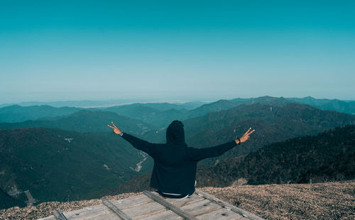 Man with arms raised on mountain against sky