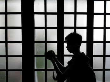 Side view of man photographing while standing by window