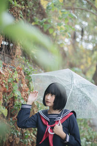 Woman standing by plants with umbrella during rainy season