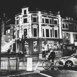 Man riding bicycle on street against buildings at night