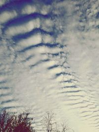 Low angle view of bare trees against cloudy sky