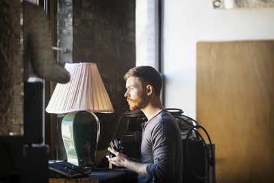 Man with camera looking away while standing at home