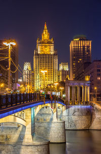 Illuminated bridge over river against buildings at night