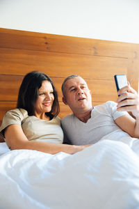 Mature couple taking selfie while sitting in bed at home
