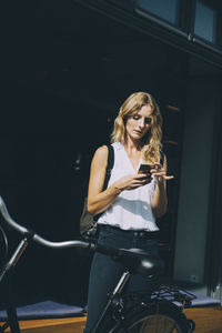 Young businesswoman using mobile phone while standing with bicycle in city
