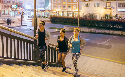 Women friends training running up stairs in city at night