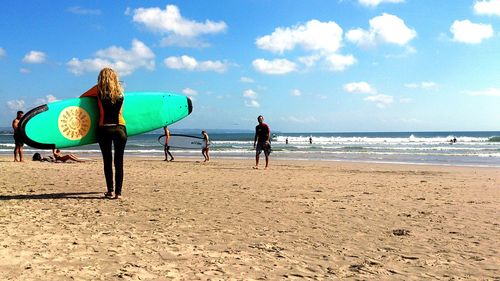 Rear view of woman holding surfboard at beach against sky