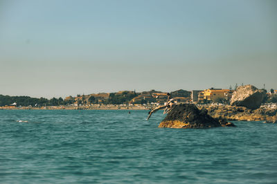 Sailboats in sea by buildings against clear sky