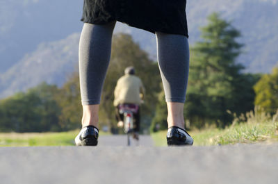 Low section of woman standing on road while man riding bicycle