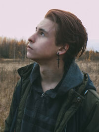 Portrait of young man looking away while standing on field