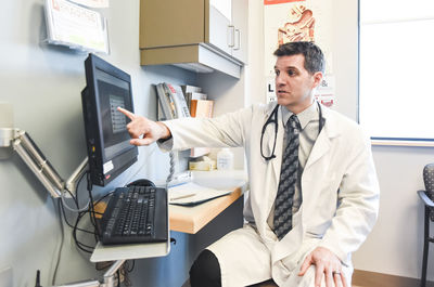 Doctor in white coat pointing at computer screen in a clinic room.