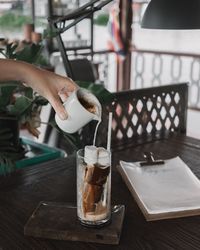 Close-up of hand pouring coffee in glass with marshmallows on table