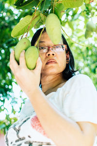 Portrait of woman holding mango growing on tree