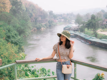 Young woman standing by railing against trees