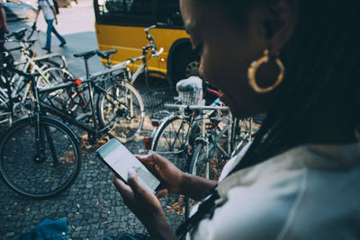 Young woman text messaging through smart phone while standing on sidewalk in city