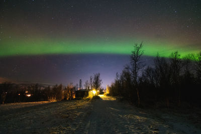 Northern lights arching over rural road at night