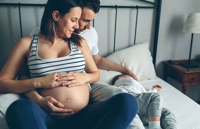 Close-up of man and woman sitting with baby on bed at home