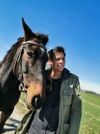 Portrait of young man with horse on field against sky