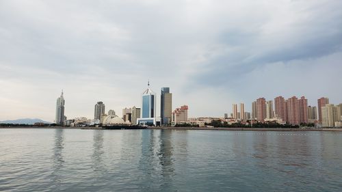 Sea by modern buildings against sky in city