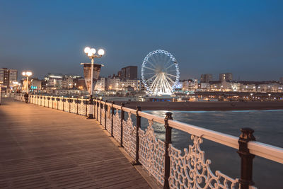 Illuminated city by sea against clear sky at night