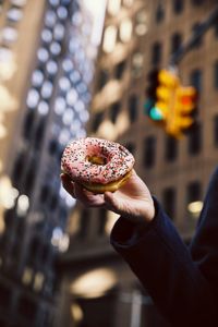 Close-up of hand holding donut against buildings